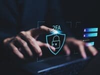 Człowiek trzymający ręce na klawiaturze laptopa i hologramy symbolizujące bezpieczeństwo oraz system 2FA