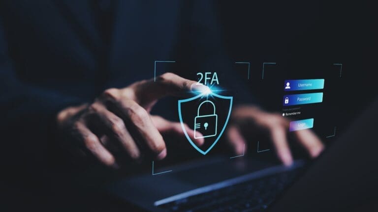 Człowiek trzymający ręce na klawiaturze laptopa i hologramy symbolizujące bezpieczeństwo oraz system 2FA